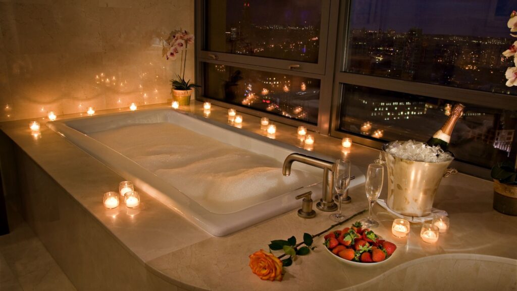 In-room jacuzzi surrounded by candles, champagne, and city views, prepared for a romantic evening